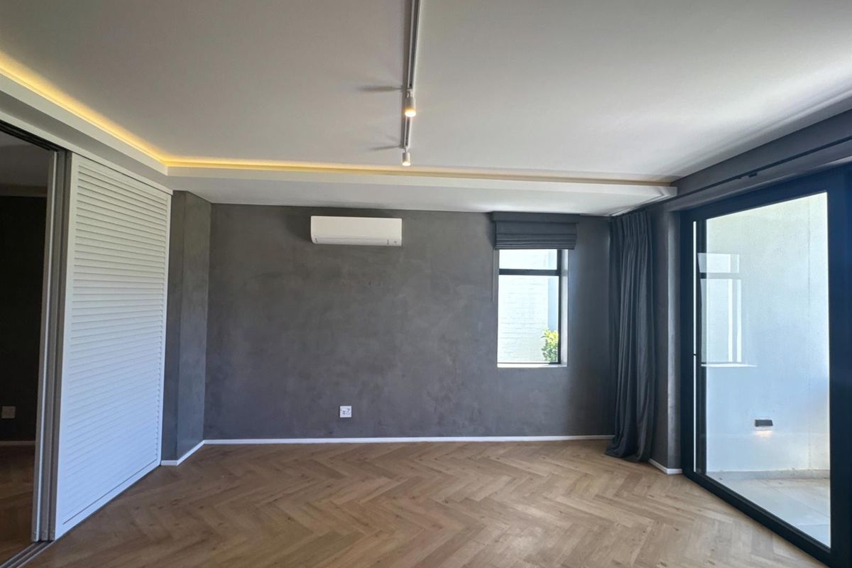 Modern living area featuring herringbone timber flooring, recessed cove lighting, track lighting, and a split-system air conditioner, with access to an outdoor space.