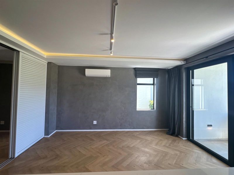 Modern living area featuring herringbone timber flooring, recessed cove lighting, track lighting, and a split-system air conditioner, with access to an outdoor space.