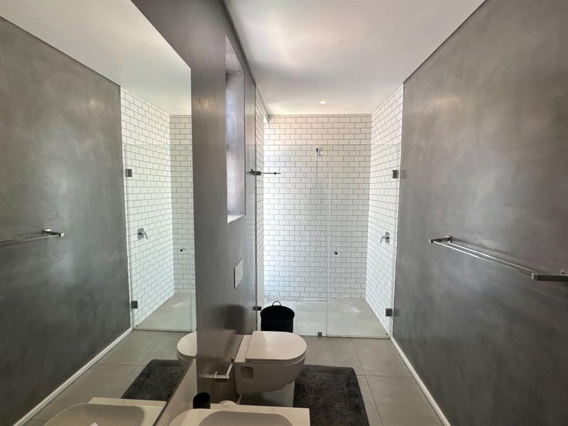 Modern bathroom featuring a walk-in shower with subway tiling, wall-mounted toilet, and large vanity mirror with contemporary grey wall finishes.