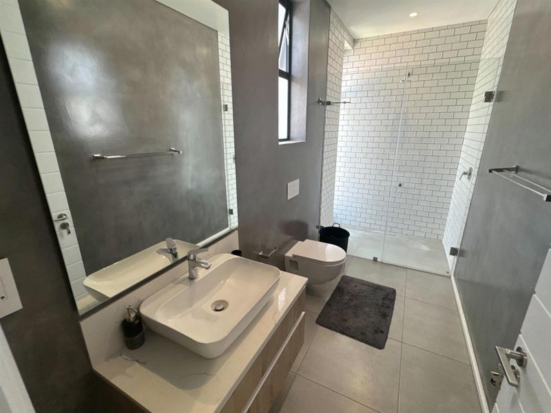 Modern bathroom featuring a wall-mounted vanity with vessel sink, wall-hung toilet, and a spacious walk-in shower with white subway tiling.