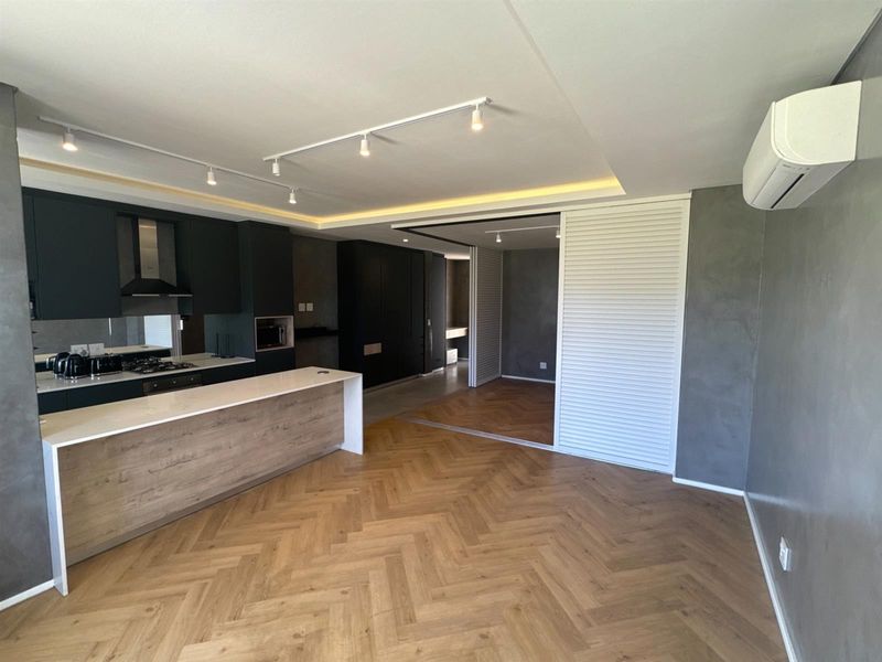Modern open-plan living area featuring herringbone timber flooring, a sleek kitchen island, built-in cabinetry, and a split-system air conditioner in a contemporary neutral palette.