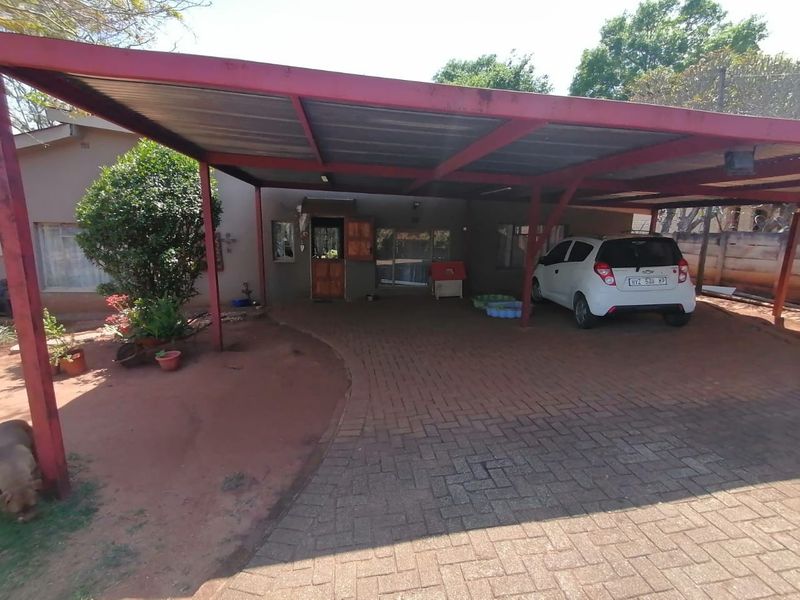 Front elevation of the house featuring a large covered carport and a paved driveway leading to the main entrance.