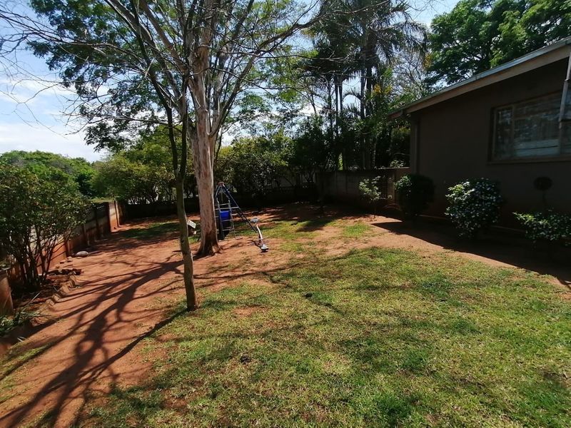 A spacious rear garden area featuring mature trees, boundary walls, and a mix of lawn and exposed soil.