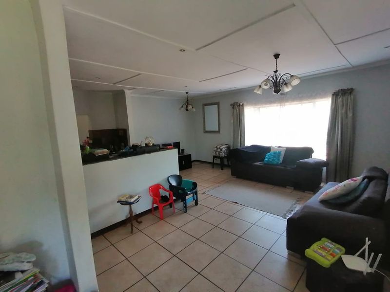 An open-plan living area featuring tiled flooring and a partial wall separating the kitchen space, with visible ceiling paneling and natural light.
