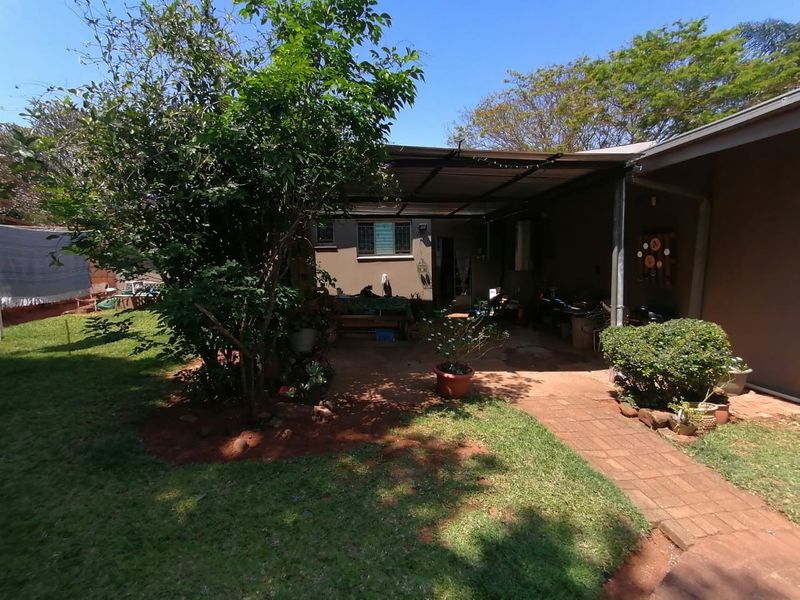 A covered outdoor patio area featuring a paved walkway leading to a garden space with established trees and lawn.