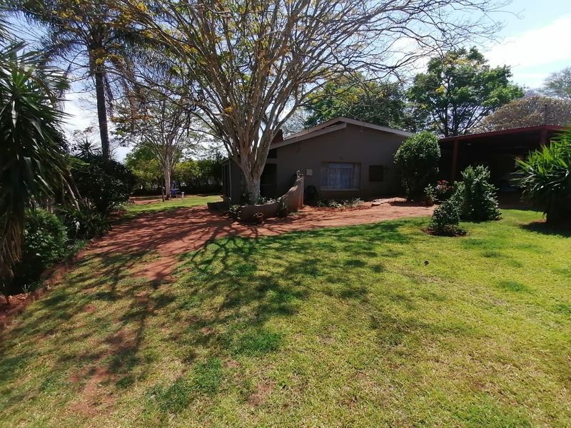 A view of the rear exterior of the house featuring a spacious garden, mature trees, and an attached carport area.
