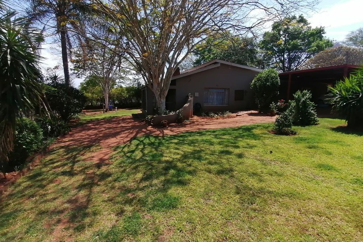 A view of the rear exterior of the house featuring a spacious garden, mature trees, and an attached carport area.