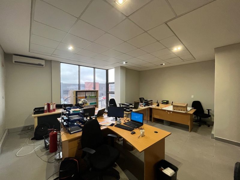 A functional office space featuring a suspended ceiling, recessed lighting, an integrated air conditioning unit, and large windows providing natural light.