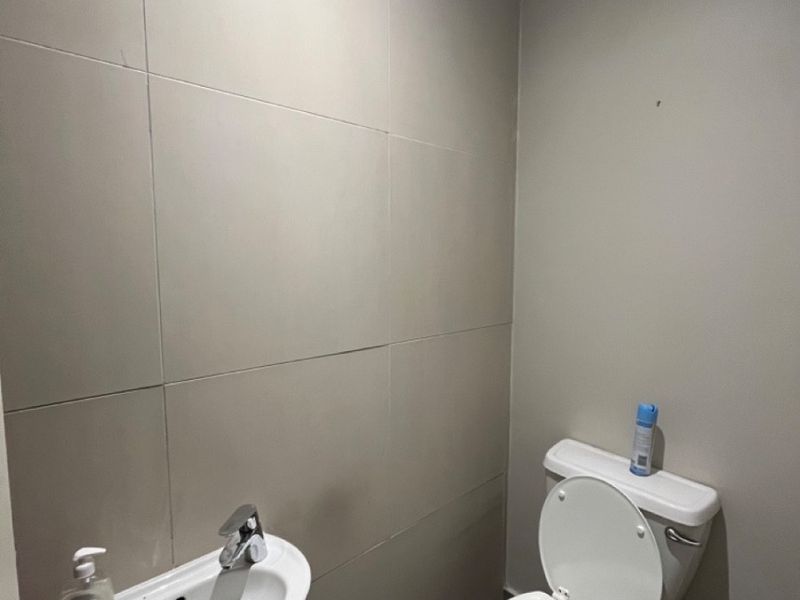 A compact, functional bathroom featuring a pedestal sink, toilet, and neutral wall tiling.