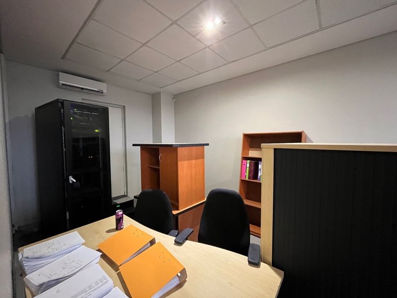 A functional office space featuring a suspended ceiling, recessed lighting, and a wall-mounted split-system air conditioning unit.