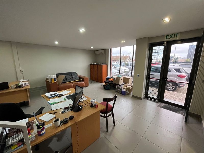 Open-plan office space featuring large glass windows, tiled flooring, recessed lighting, and a wall-mounted air conditioning unit.