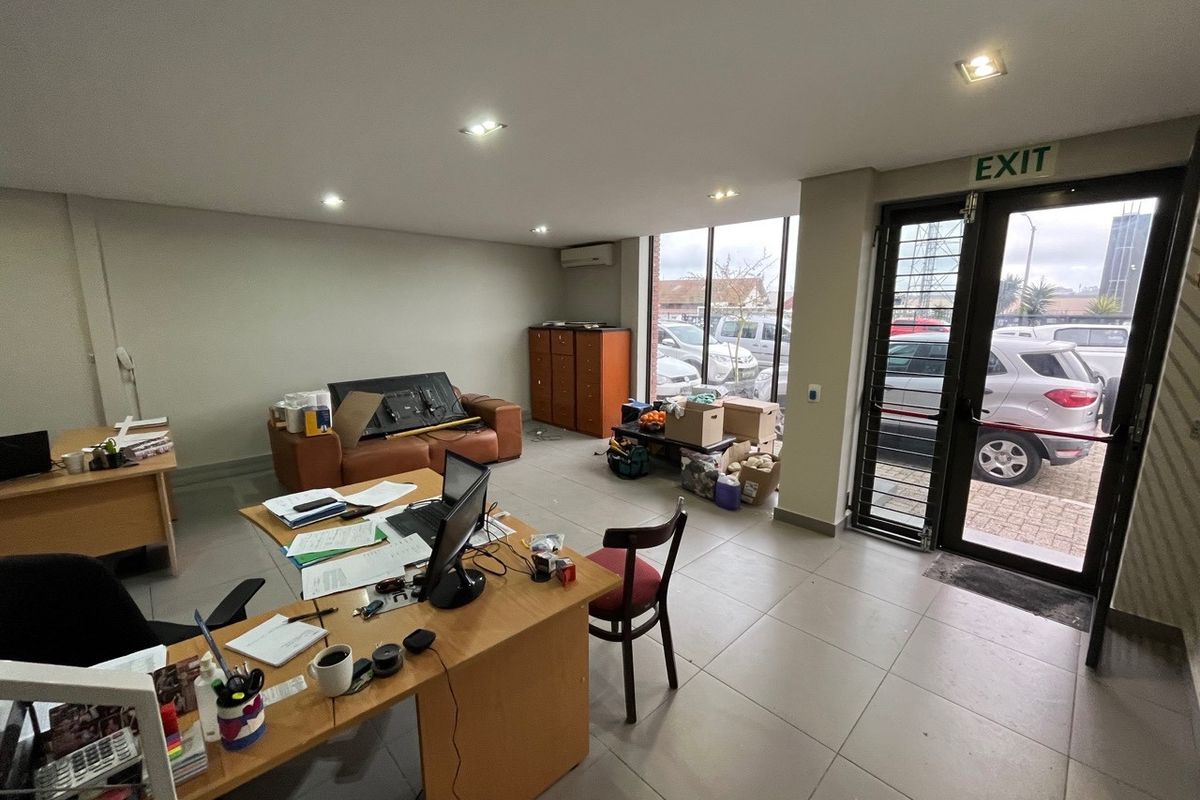 Open-plan office space featuring large glass windows, tiled flooring, recessed lighting, and a wall-mounted air conditioning unit.