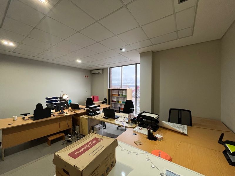 A functional office space featuring a suspended ceiling, recessed lighting, air conditioning, and large windows providing natural light.