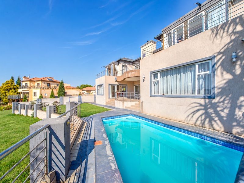 Rear exterior view of a multi-story house featuring a swimming pool, tiled patio area, and upper-level balconies with stainless steel railings.