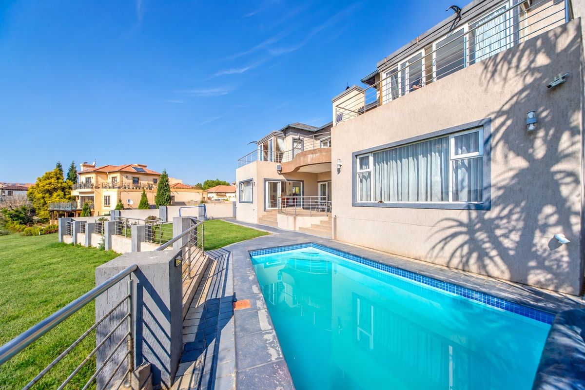 Rear exterior view of a multi-story house featuring a swimming pool, tiled patio area, and upper-level balconies with stainless steel railings.