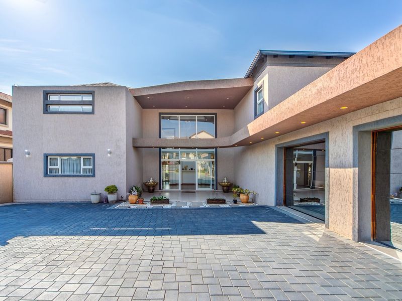 Modern double-storey home featuring a spacious paved driveway, large glass entrance, and integrated garage with recessed exterior lighting.