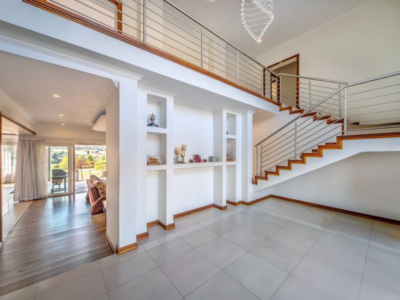 Spacious double-volume entrance hall featuring a modern staircase with stainless steel balustrades, tiled flooring, and elegant built-in wall niches.
