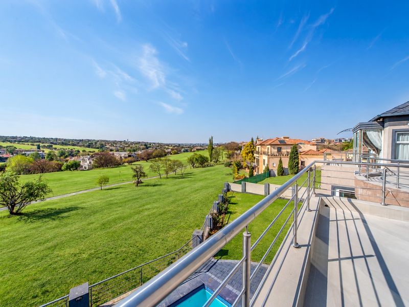 Spacious elevated balcony featuring a modern stainless steel balustrade, offering expansive views over the manicured estate grounds and swimming pool below.