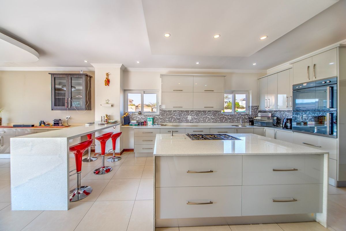 Modern kitchen featuring a large central island with gas hob, breakfast bar, built-in oven, and sleek cabinetry with quartz countertops.