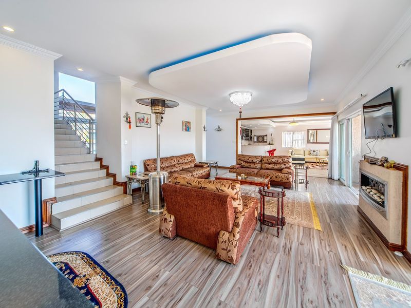 Spacious open-plan living area featuring wood-look flooring, a modern recessed ceiling with cove lighting, a built-in fireplace, and direct access to a staircase.