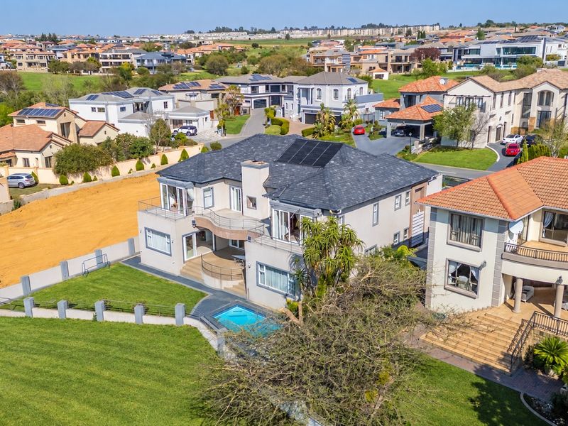 Aerial view of a residential property featuring a swimming pool, balcony, and solar panels, situated within a suburban estate.