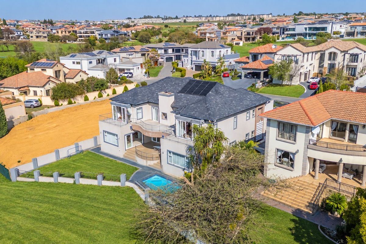 Aerial view of a residential property featuring a swimming pool, balcony, and solar panels, situated within a suburban estate.
