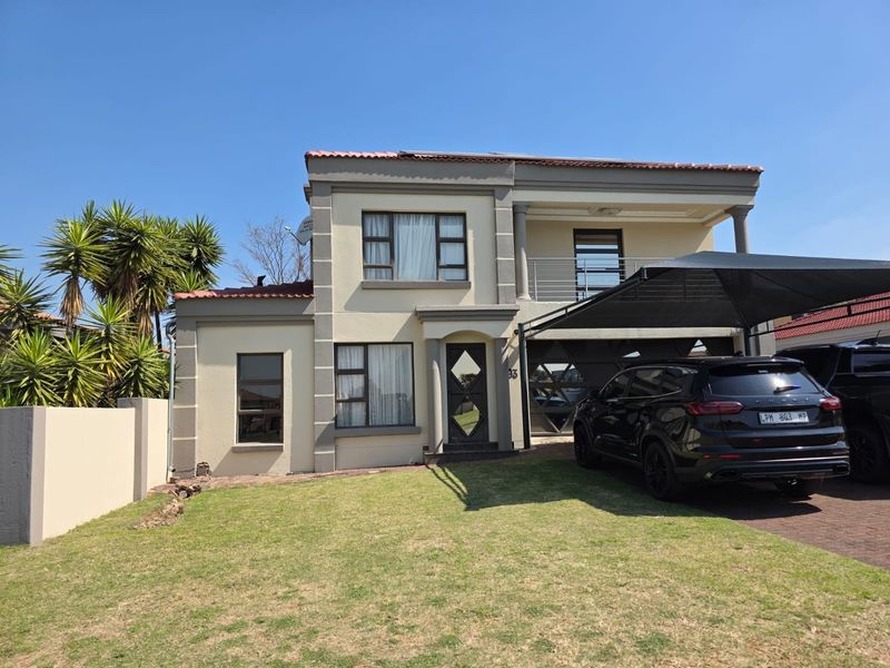 A well-maintained double-story residential home featuring a paved driveway, shade cloth carport, balcony, and a neat front garden.