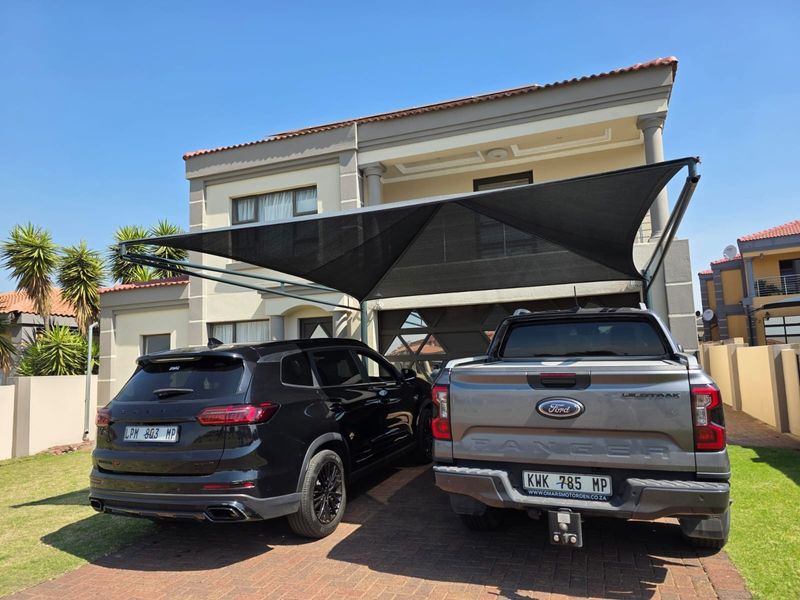 Front elevation of a two-story house featuring a paved driveway, double garage, and a large installed shade sail structure.