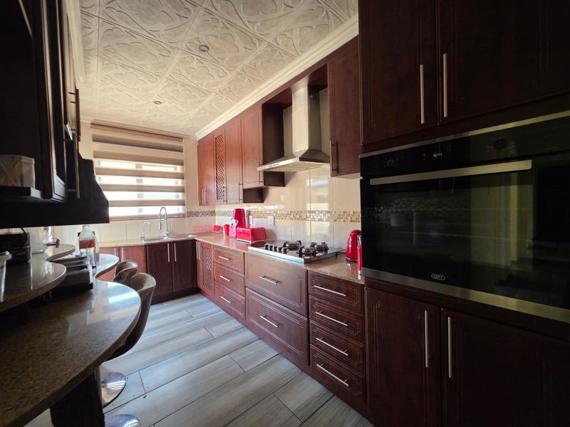 A well-appointed kitchen featuring dark wood cabinetry, granite countertops, integrated appliances, and decorative ceiling tiles, offering a functional and stylish cooking space.