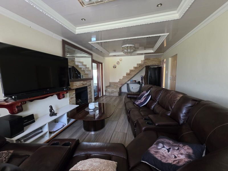 Spacious living room featuring a stone-clad fireplace, decorative recessed ceiling with cove lighting, and a staircase leading to the upper level.