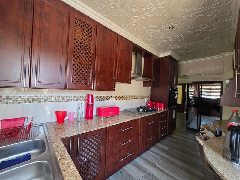 A well-maintained kitchen featuring dark wood cabinetry, granite countertops, a gas hob with extractor, and decorative ceiling tiles.
