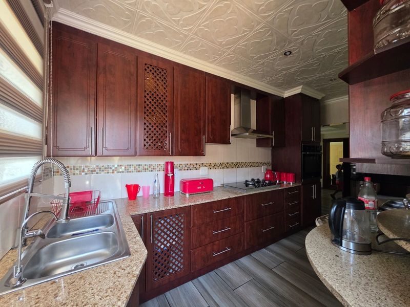 A well-appointed kitchen featuring dark wood cabinetry, granite countertops, a gas hob with extractor, and decorative ceiling tiles, offering a functional and classic aesthetic.