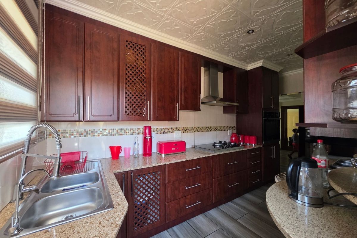 A well-appointed kitchen featuring dark wood cabinetry, granite countertops, a gas hob with extractor, and decorative ceiling tiles, offering a functional and classic aesthetic.