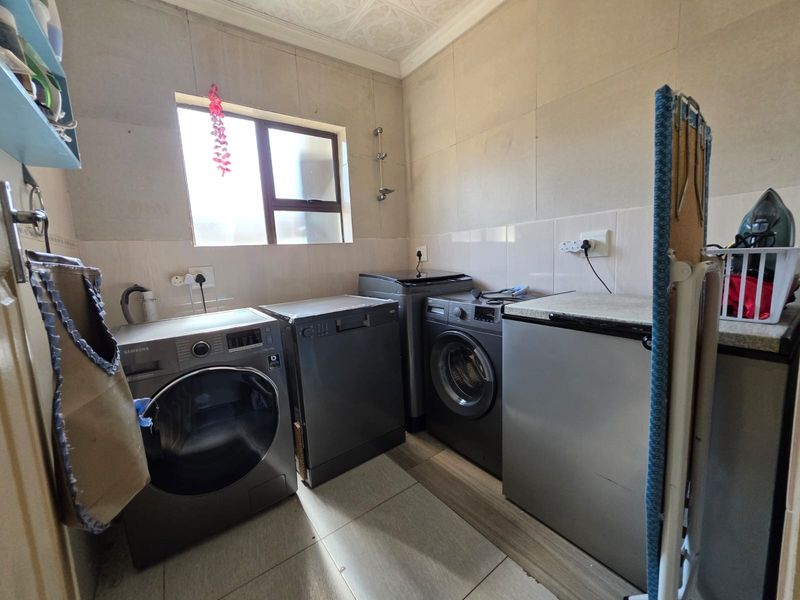 A functional laundry room featuring tiled walls, tiled flooring, and dedicated plumbing and electrical connections for multiple appliances.