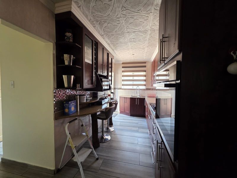 A functional kitchen featuring dark wood cabinetry, granite countertops, a mosaic backsplash, and unique decorative ceiling tiles with integrated appliances.