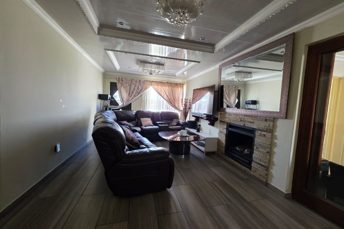 A well-maintained living room featuring a stone-clad fireplace, decorative recessed ceiling with crown molding, and modern wood-look tiled flooring.