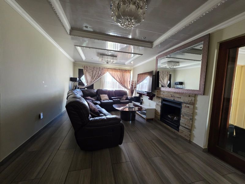 A well-maintained living room featuring a stone-clad fireplace, decorative recessed ceiling with crown molding, and modern wood-look tiled flooring.