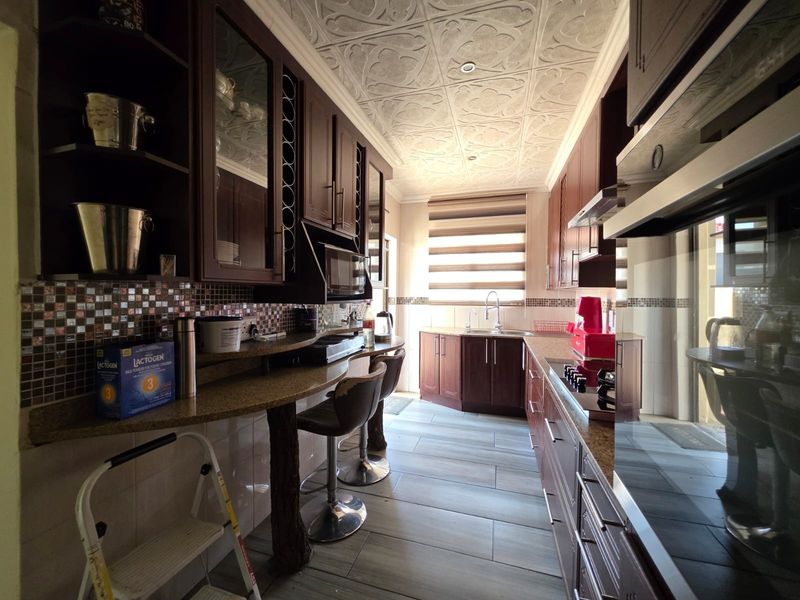 A well-appointed kitchen featuring dark wood cabinetry, granite countertops, mosaic tile backsplash, and unique decorative ceiling tiles with integrated appliances.