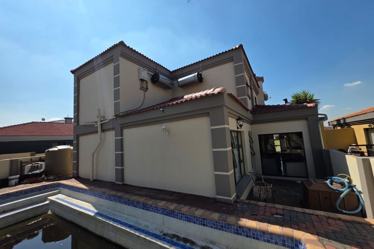 Rear view of the property featuring a swimming pool, paved patio area, and exterior solar water heating system.