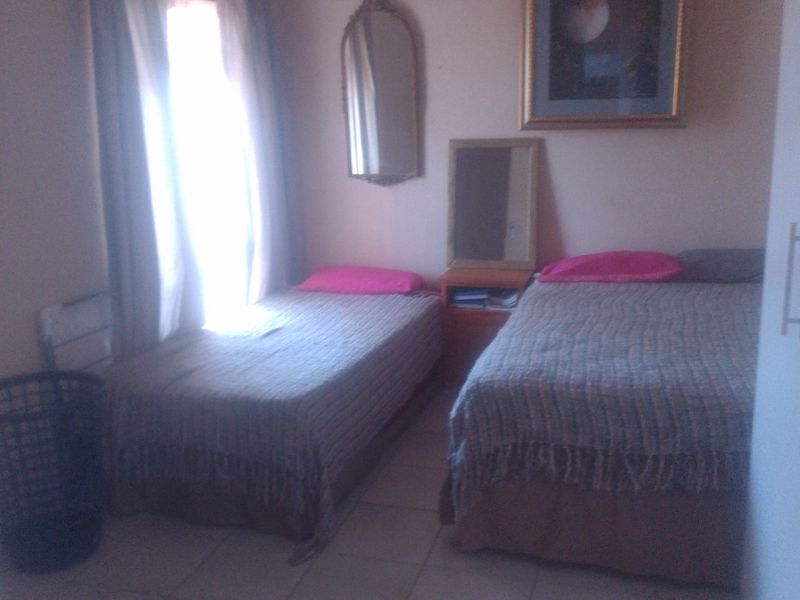 A bedroom featuring tiled flooring and a ceiling fan, with natural light entering through the window.