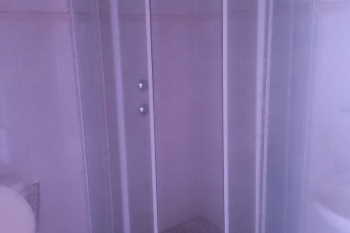 A functional bathroom featuring a corner shower enclosure with glass doors, tiled flooring, and wall tiling.