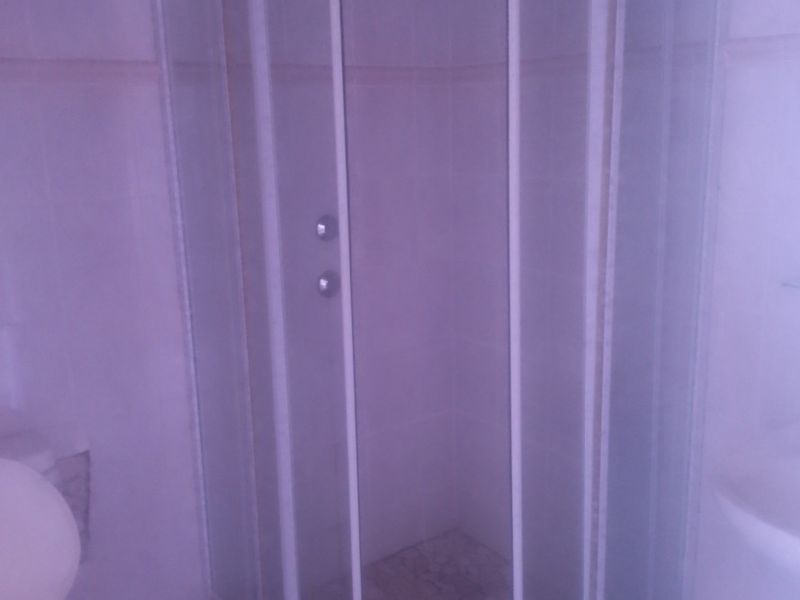 A functional bathroom featuring a corner shower enclosure with glass doors, tiled flooring, and wall tiling.