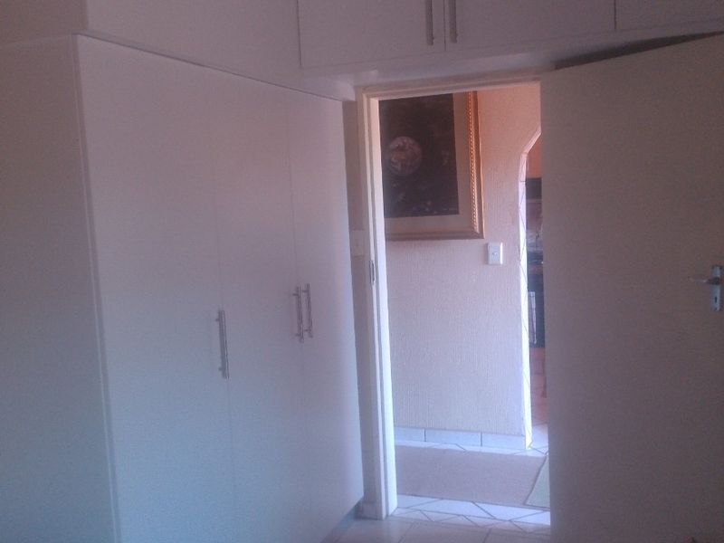 Bedroom featuring built-in cupboards with overhead storage and tiled flooring, leading into an adjacent hallway area.