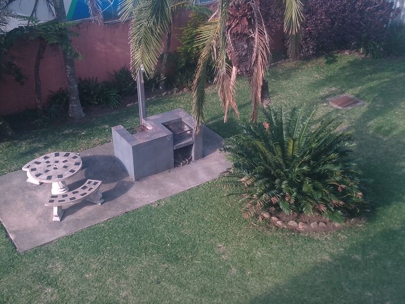 An elevated view of a private garden area featuring a built-in braai and a concrete patio space.