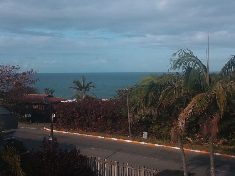 An elevated view overlooking a coastal road with lush tropical vegetation and a clear ocean horizon in the background.