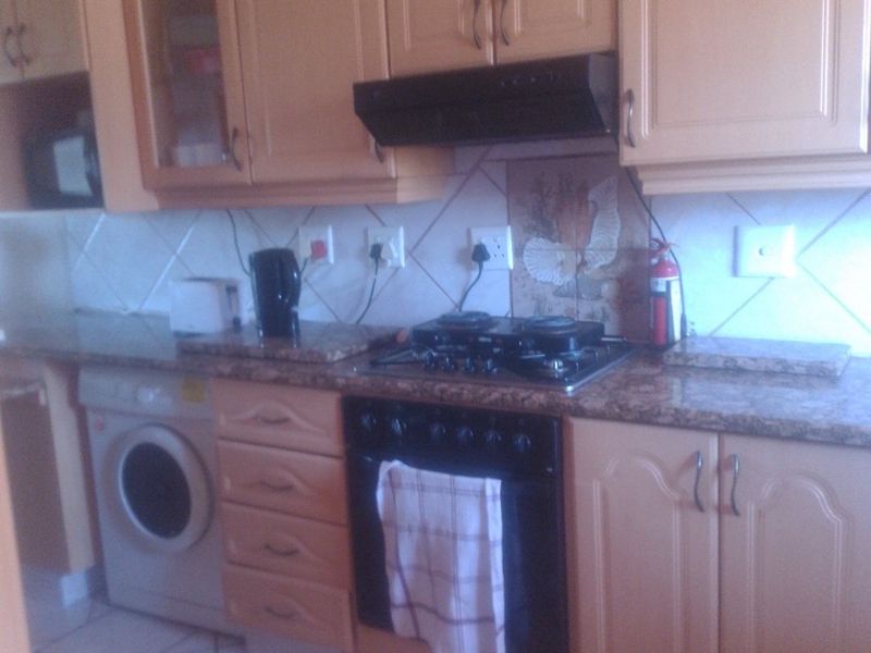 A functional kitchen featuring light wood cabinetry, granite countertops, a gas hob, built-in oven, and tiled flooring.