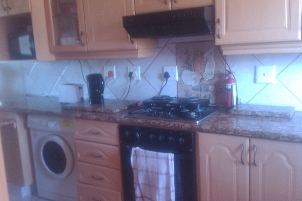 A functional kitchen featuring light wood cabinetry, granite countertops, a gas hob, built-in oven, and tiled flooring.