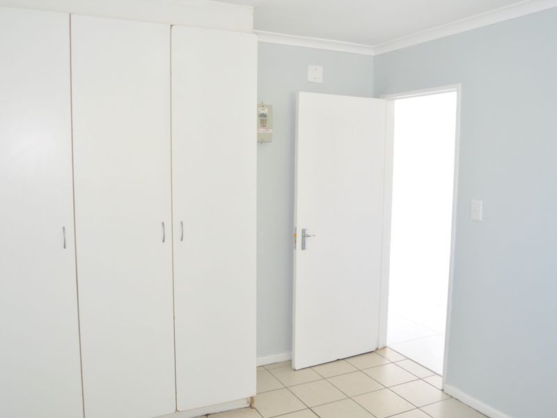 A bright, empty bedroom featuring built-in cupboards, neutral tiled flooring, and light-colored walls, offering a clean canvas for personalization.