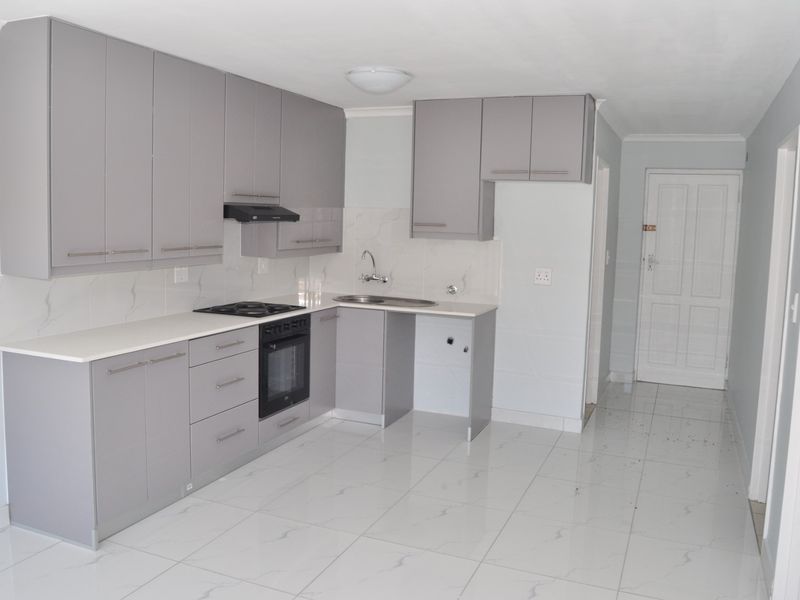 A modern, clean kitchen featuring grey cabinetry, a gas hob, built-in oven, and white marble-look tiled flooring in an open-plan layout.