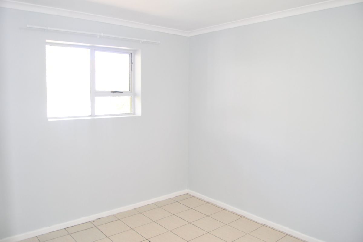 A bright, empty bedroom featuring neutral wall paint, tiled flooring, and a functional sliding window with an installed curtain rod.